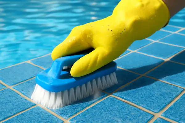 person scrubbing pool tiles